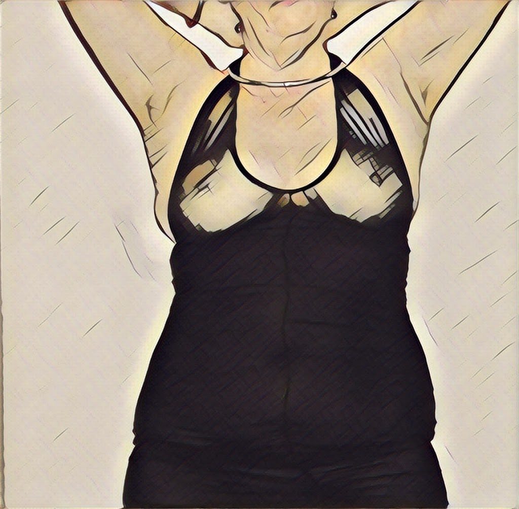 A modified of me standing with my hands behind my neck. You can see my breasts through the black halter neck dress and I am wearing my collar. 