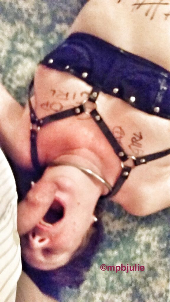 I am lying on my back. Wearing a framed bra. There is writing on my body - good girl, plus tally lines denoting orgasms. My mouth is open and Master's cock hovers above. 