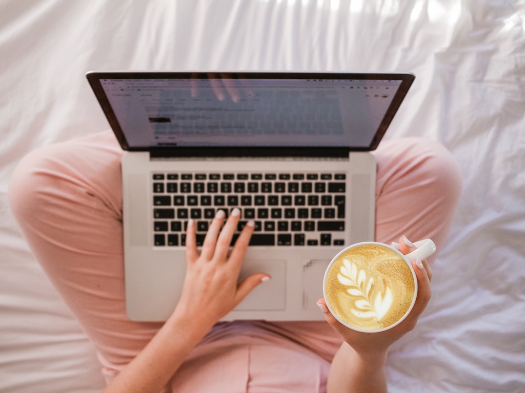 A person sitting crosslegged with a coffee and an apple MacBook. 