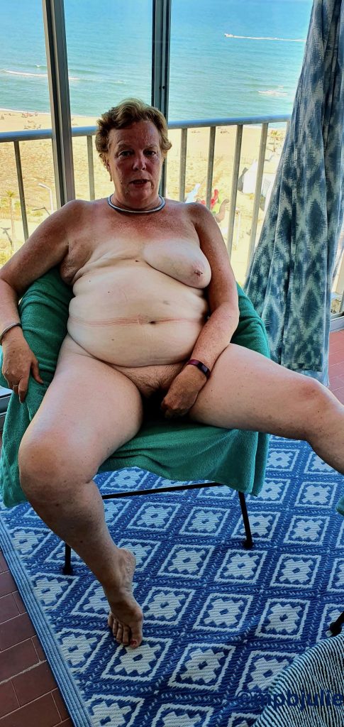 I'm sitting naked on a chair in an enclosed balcony. There is a beach view behind me.