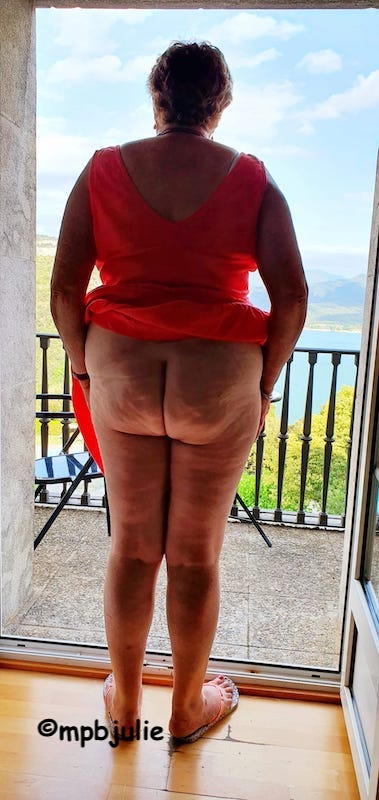 Me facing a lake from a hotel room and balcony. I'm wearing a red sun dress and my bottom is bare, 