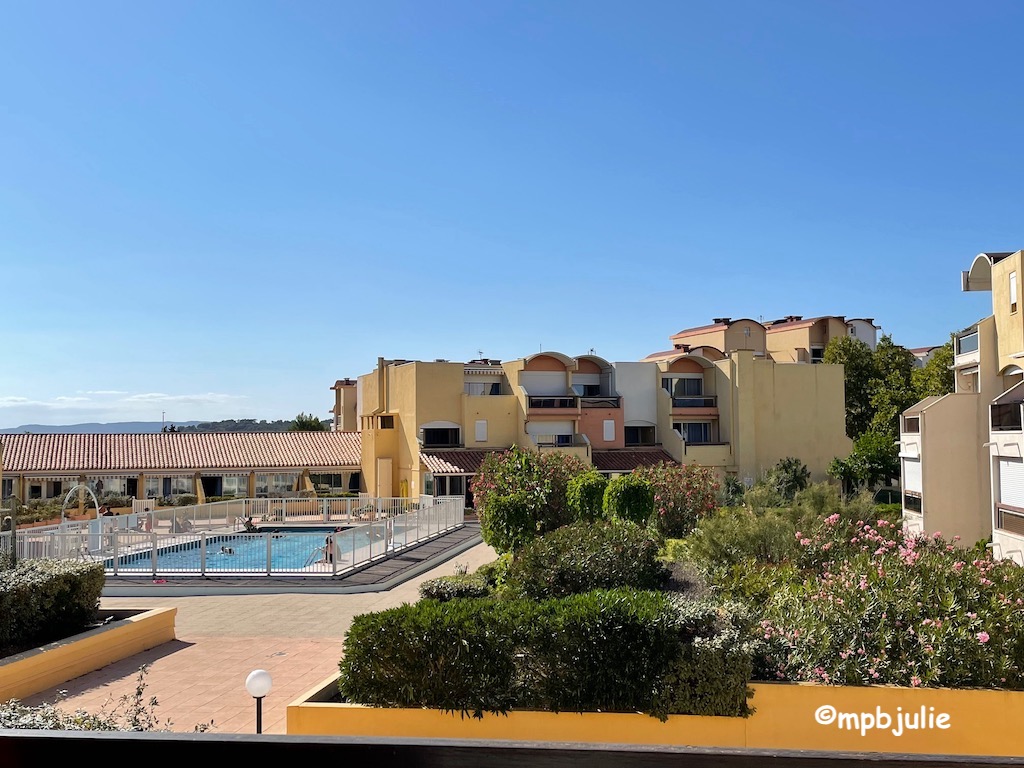 A bright sunny summer day. An apartment complex complete with swimming pool. People are in and on the edge of the pool.