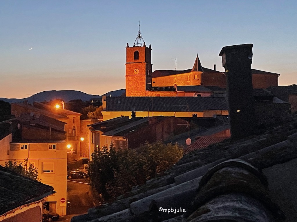 It's sunset and in the distance across the rooftrees of our terrace you can see houses, trees and a large church / castle like building. In fact it's the town hall and while there is a bell tower it isn't the church. Lights glow and make the buildings shine brown against the clear darkening blue sky