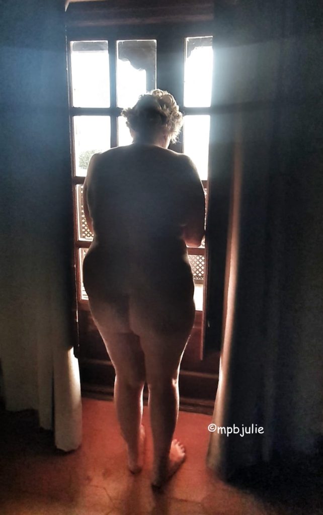 I am standing in a semi dark room, facing into the light of the window. I am naked