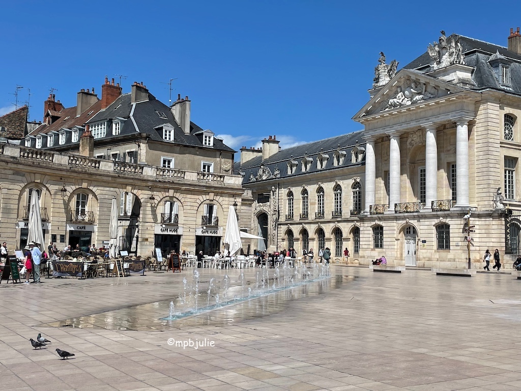 The centre of Dijon. Buildings against a blue cloudless sky. Fountains in foreground
