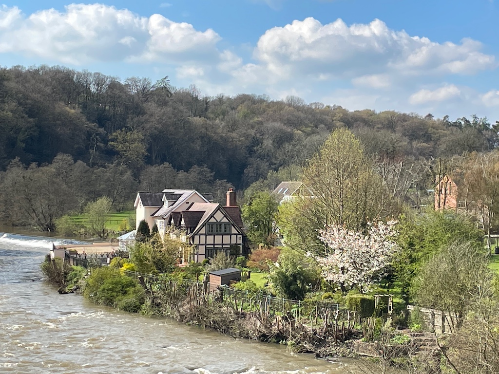 Ludlow. Trees in background. House and garden to right and fast flowing river to left. 