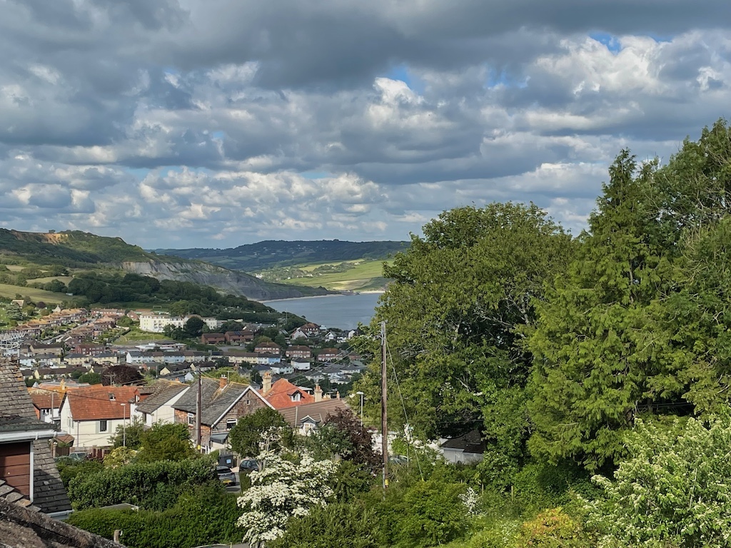 View across countryside. Houses in foreground, trees to light and far distance and then a small amount of sea in the middle.
