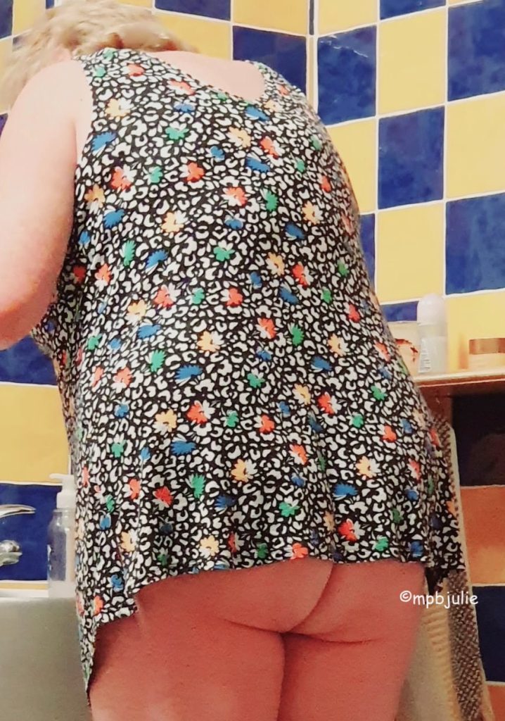I am standing in the bathroom of our holiday home in France cleaning my teeth. I'm wearing a multicoloured top but am bottomless