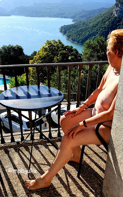 I'm sitting naked on a chair on a balcony overlooking a lake in Vic in the Pyrenees. Side ways on. 