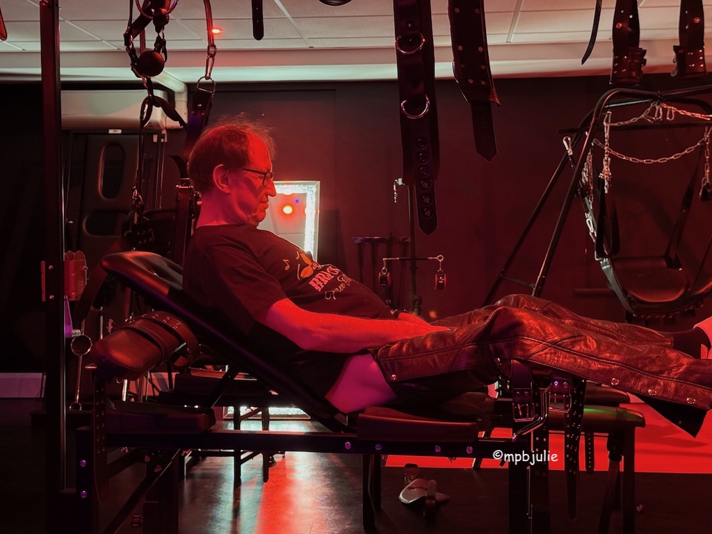 G sitting on one of the benches. He's wearing his chaps and a tee shirt.